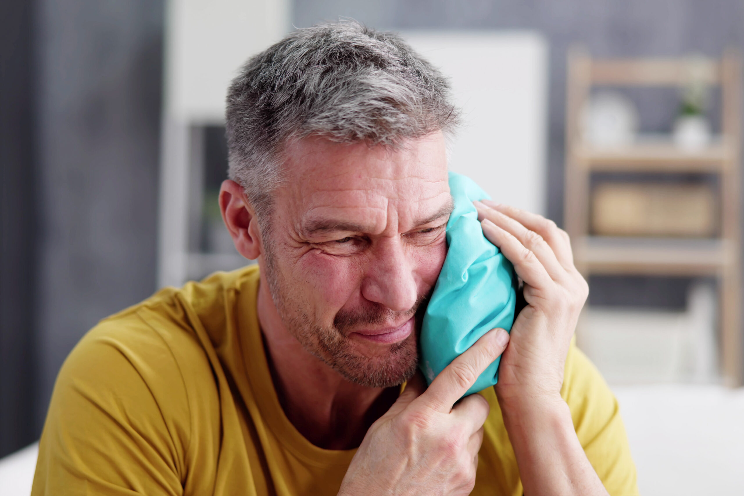 Upset Man Touching Cheek With Cold Water Bag At Home